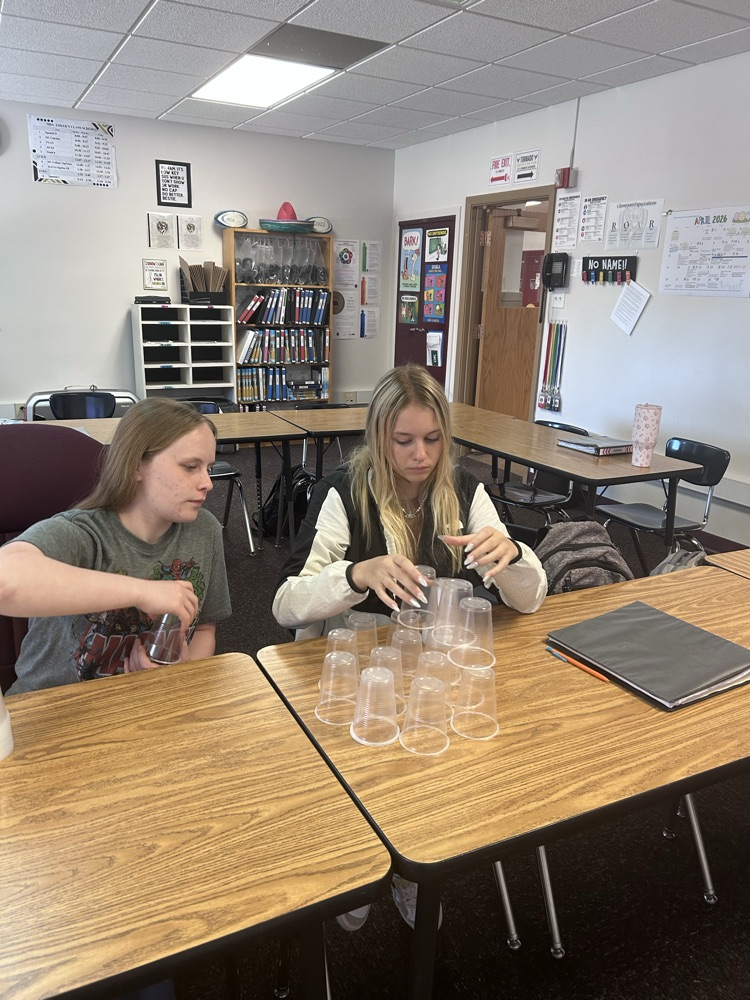 two female students sit and plan out their tower build, testing a new idea out with plastic cups