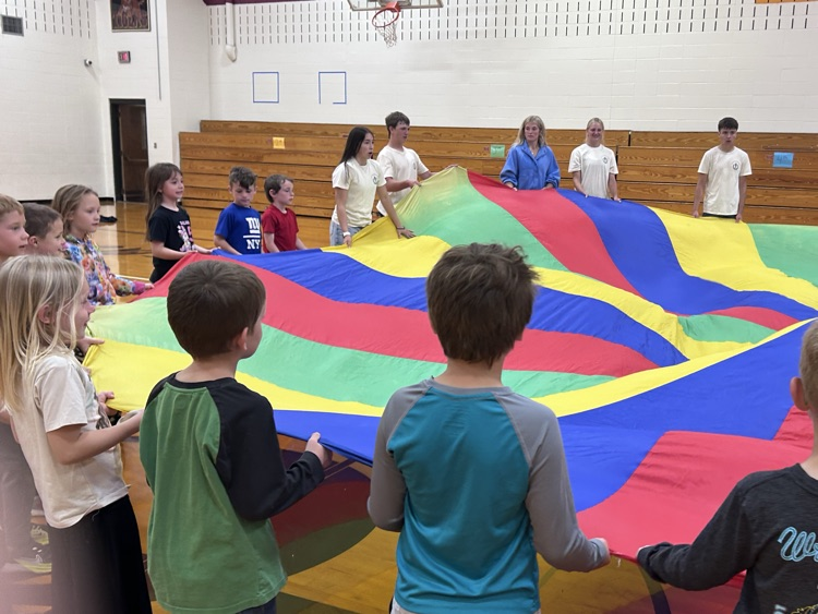 Elementary and NHS members stand around the parachute preparing to lift and sit under the dome they create