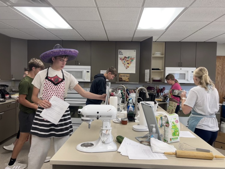 3 male students are in the left kitchen preparing their mise en place while two female students prepare their kitchen on the right