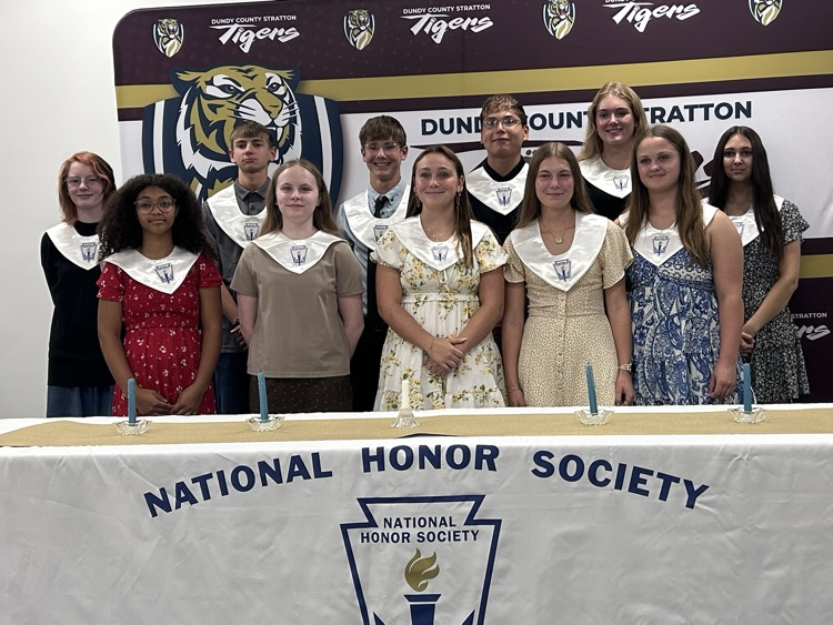 11 new inductees stand behind a table covered with a white table cloth