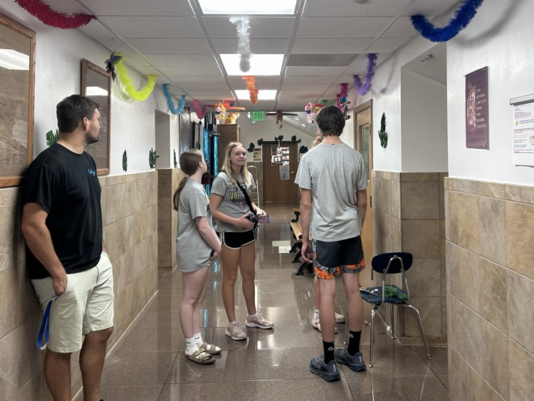 A teacher stands near a group of 4 students who are discussing plans for the rest of their decorations 