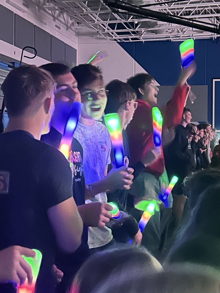 A group of four male students holding light up sticks sing and enjoy the concert