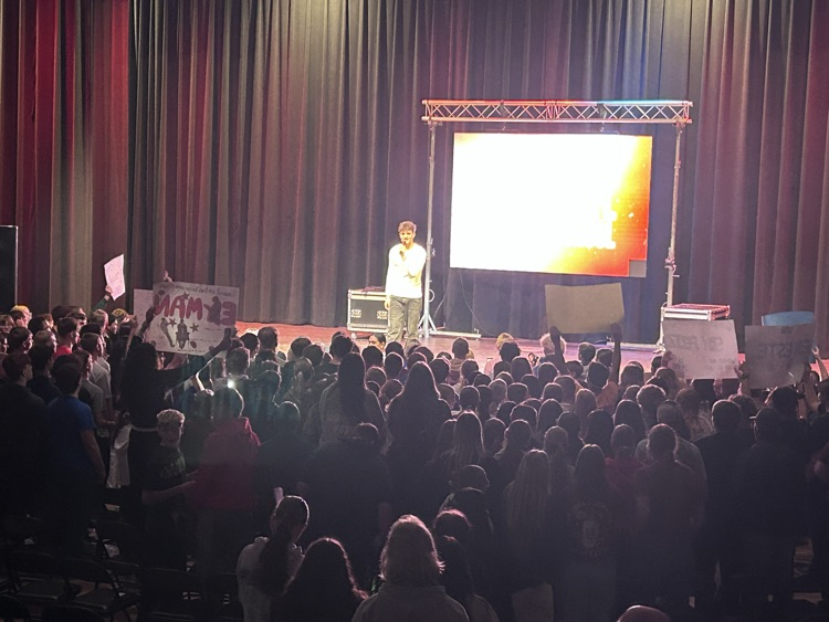 Students are grouped near the stage for the final song