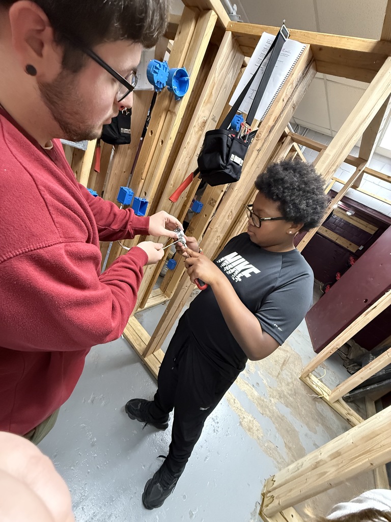 Dakota ensuring that this student makes sure his wire hooks are going in the correct direction on a duplex receptacle (outlet)