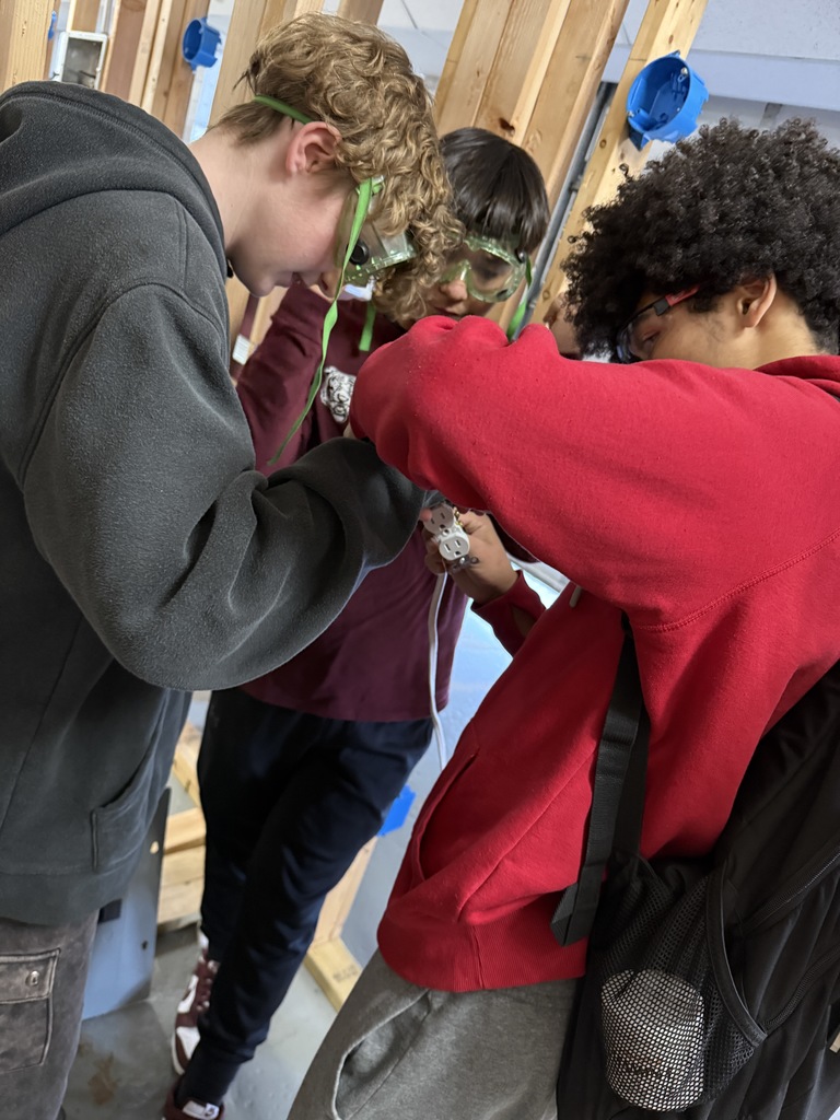 Tramar is working with two STEM students to show them how to hook a wire and secure it to a duplex receptacle (an outlet) in a clean and professional manner. 