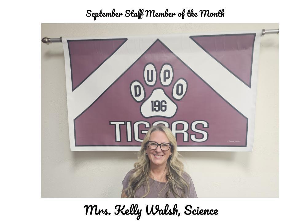 Woman smiling in front of a sign that reads, "September Staff Member of the Month" above "TIGERS" and a paw print.