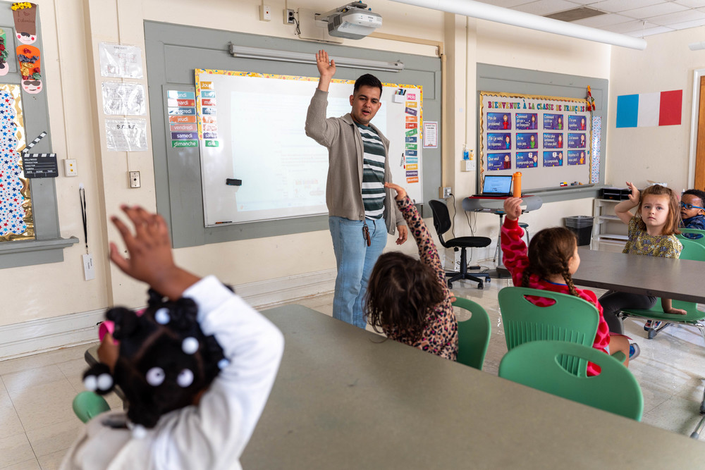 teacher leading class, kids with hands raised