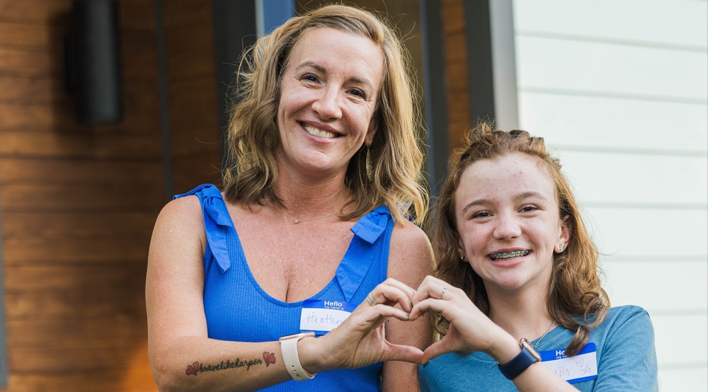 woman and child standing next to each other and holding hands to make a heart