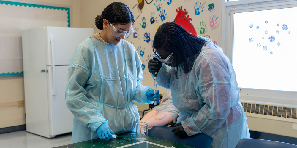 Two students in PPE pulling liquid from a beaker with an extractor