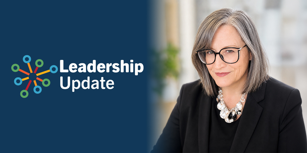 A woman with glasses and gray hair, wearing a black suit, smiles slightly. Beside her, the text reads "Leadership Update" with a colorful icon.