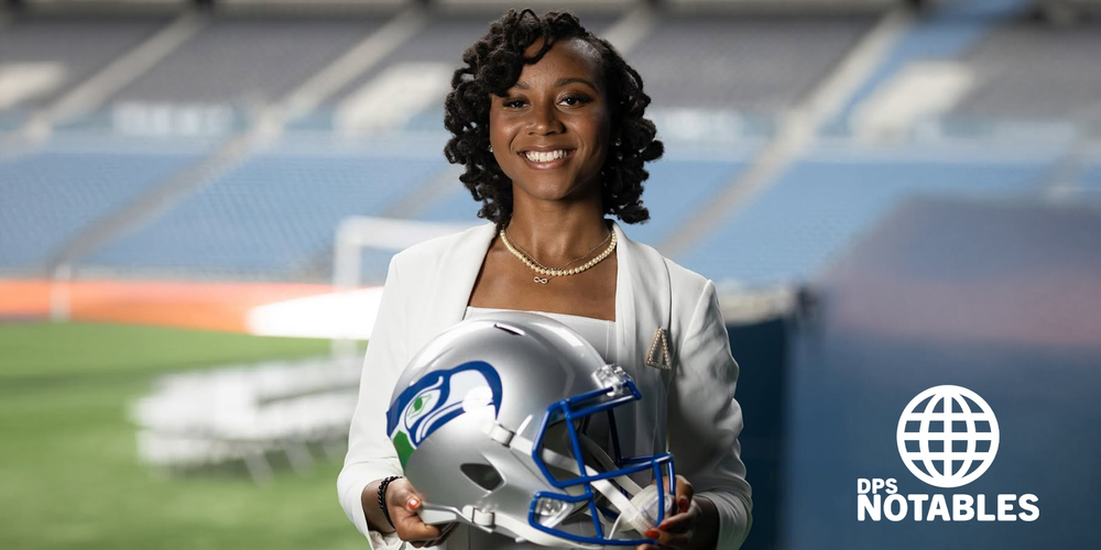Dajah Stallings in a white outfit smiles while holding a Seattle Seahawks football helmet. She's standing on a football field. The mood is professional and confident.