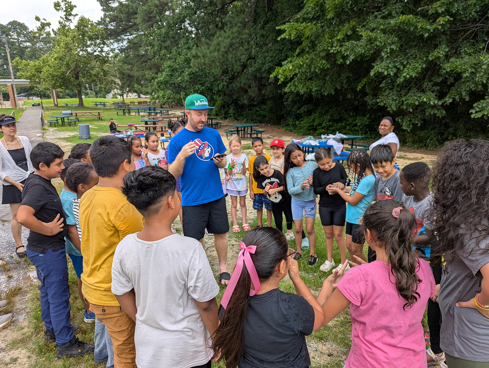 students stand in a circle around a teacher outside