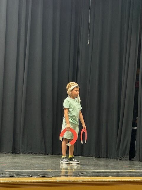 A boy standing on stage with a cardboard magnet on each hand