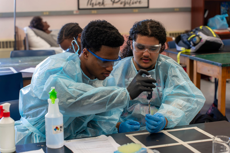 Two males in PPE using an extractor to pull liquid from a beaker