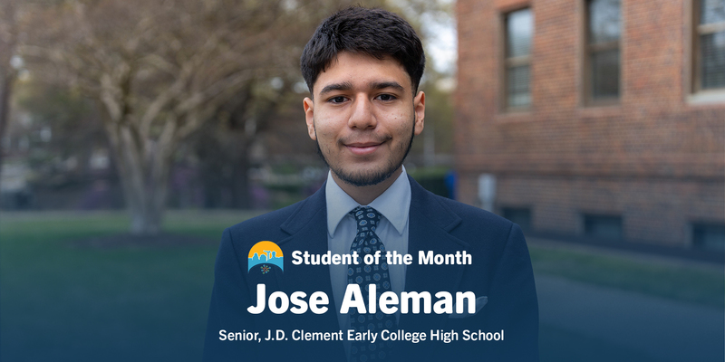 Young man in a suit and tie stands smiling outdoors with blurred trees and a brick building in the background. Text reads, "Student of the Month: Jose Aleman, Senior, J.D. Clement Early College High School."