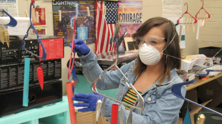 student wearing a mask, gloves, and safety goggles doing an experiment