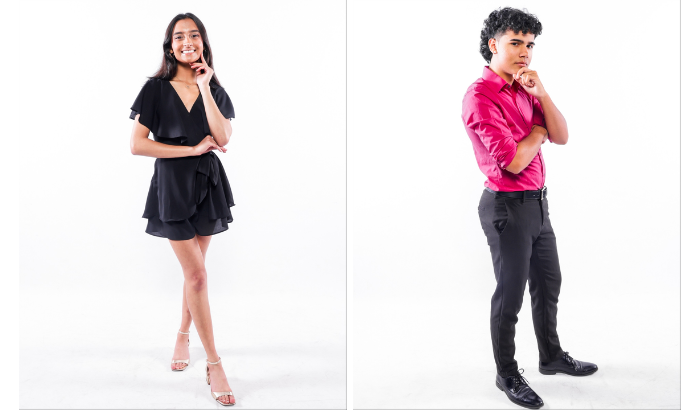 Shalya Satya and Cory McHugh, winners of Miss and Mister Atlantic Coast 2025, pose confidently against a white background. Shalya is wearing a short black ruffled dress and open-toed heels, smiling with one hand resting near her chin. Cory is wearing a bright pink dress shirt and black pants, standing with his arms folded and one hand thoughtfully resting on his chin.