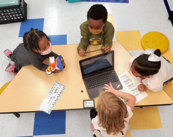 Students in masks gathered around a laptop on a desk