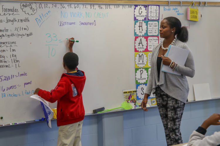 Kid doing a division in the whiteboard, teacher supervising