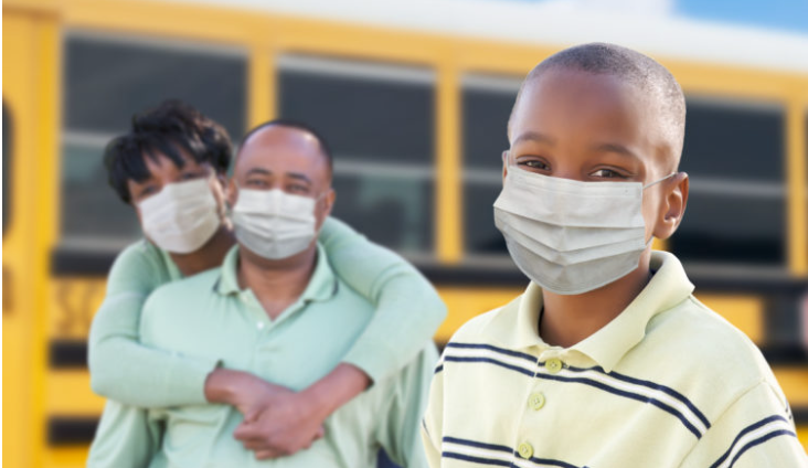 Image of a family in masks standing in front of a yellow bus