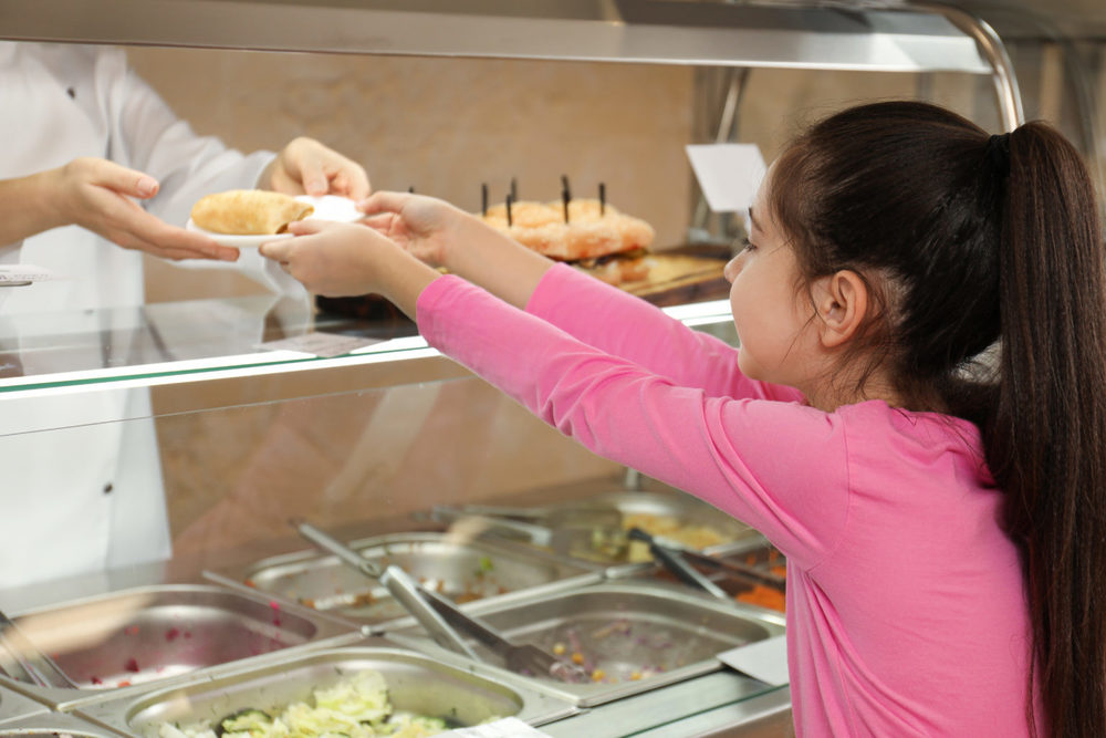 A child in a school cafeteria line reaches for a tray of food.