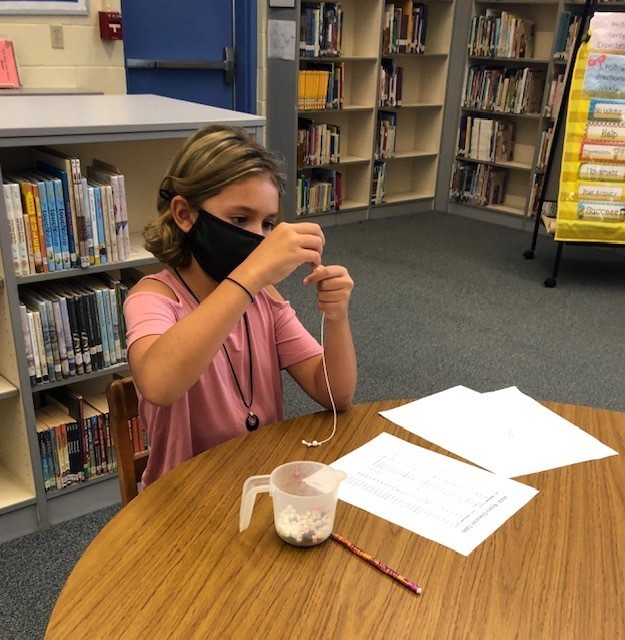 A student in a library putting beads on a string