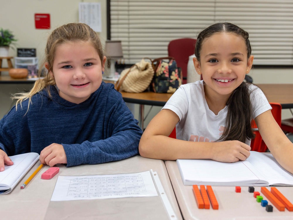 Two Crown Point Elementary students next to each other, with notebooks and paper, smiling