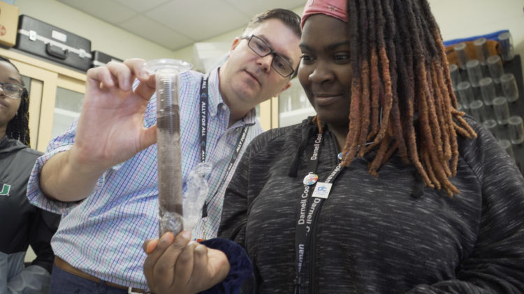 Student holds test tube, while teacher looks at it with her. 