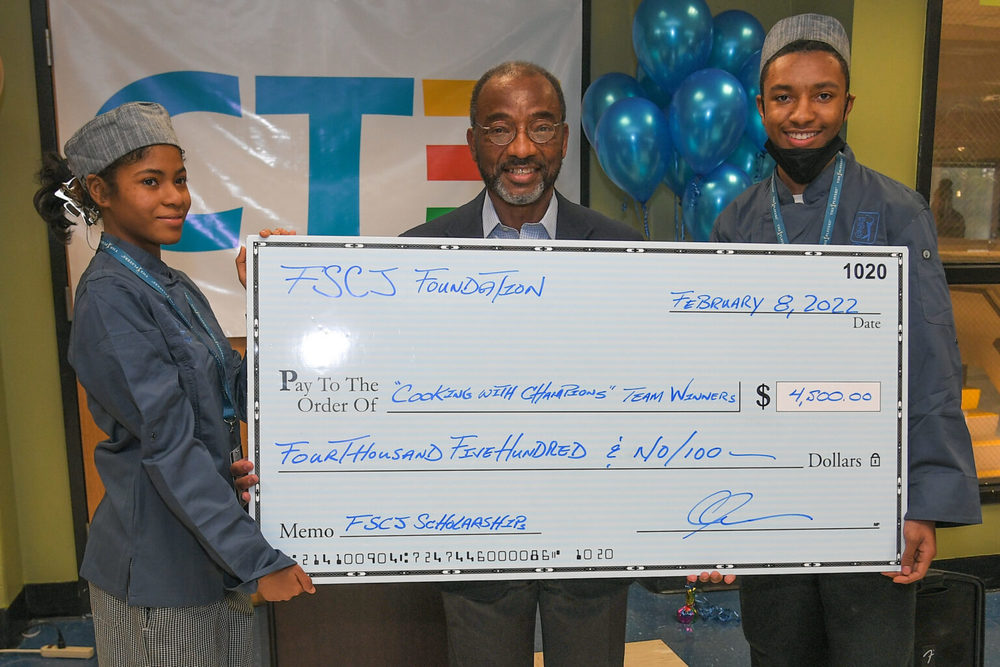 2 students and a teacher holding a check price