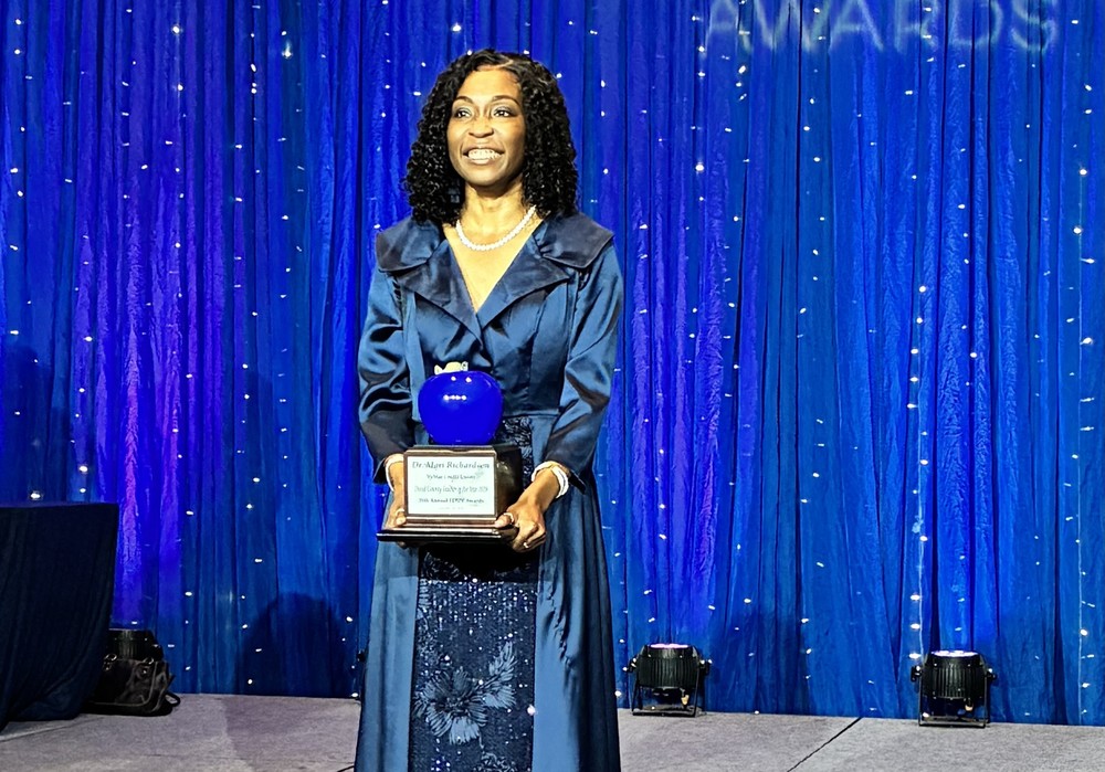 Dr. Mari Richardson smiles on stage as she holds her trophy for Teacher of the Year.