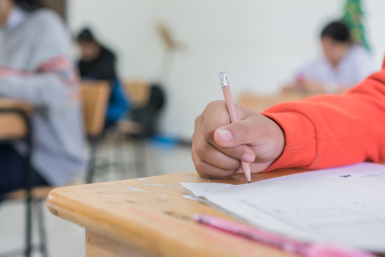Closeup of a student's hand holding a pencil and completing a worksheet. 