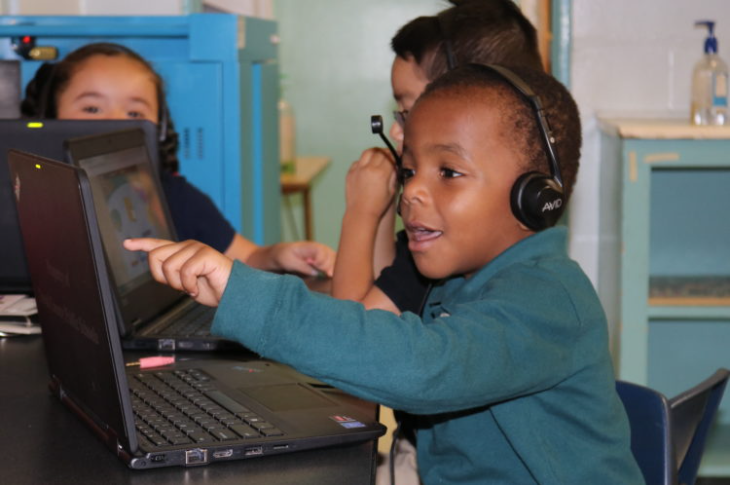 Image of a student with headphones on engaging with something on his laptop via pointing and smiling