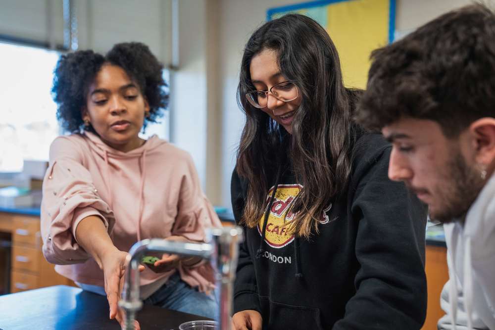 Three students stand together in a science classroom and work on a project