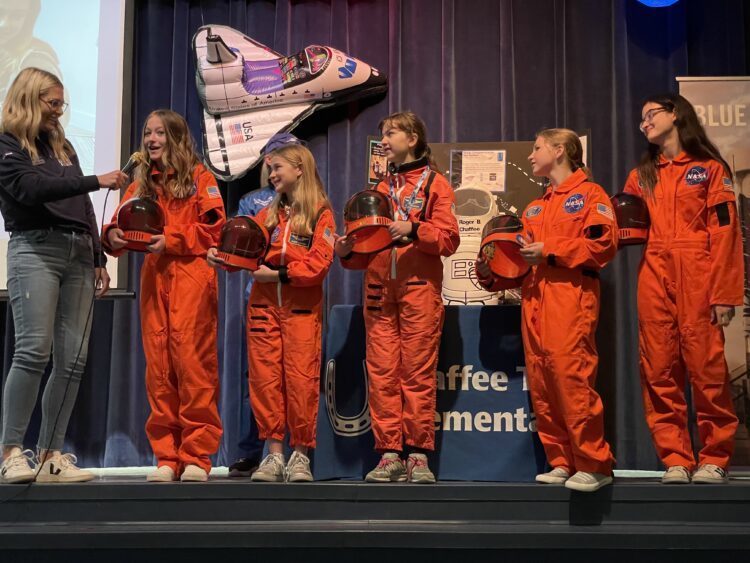 5 students dressed as astronauts speaking on stage