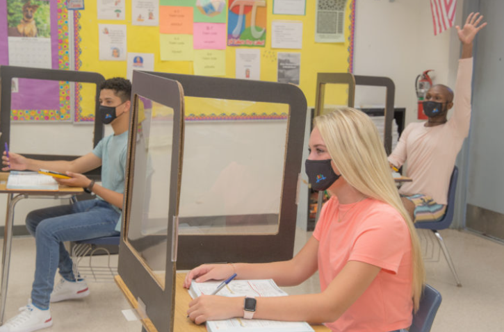 Image of students in a classroom in masks and separated by dividers.,