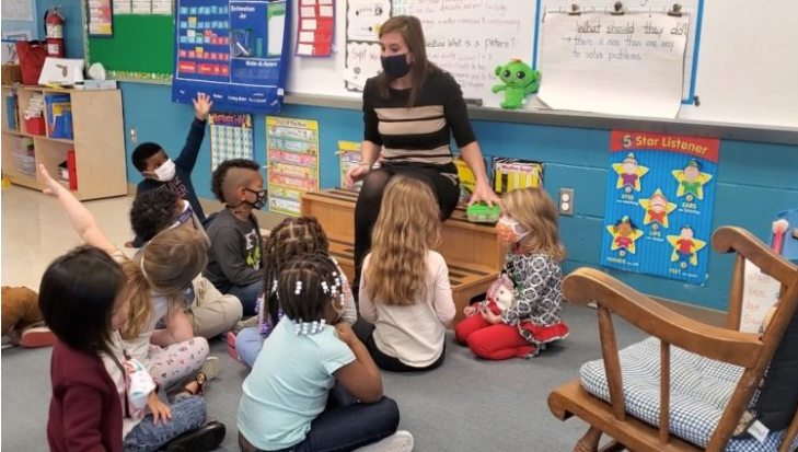 Image of a teacher in a speaking to students,  who all are in  masks