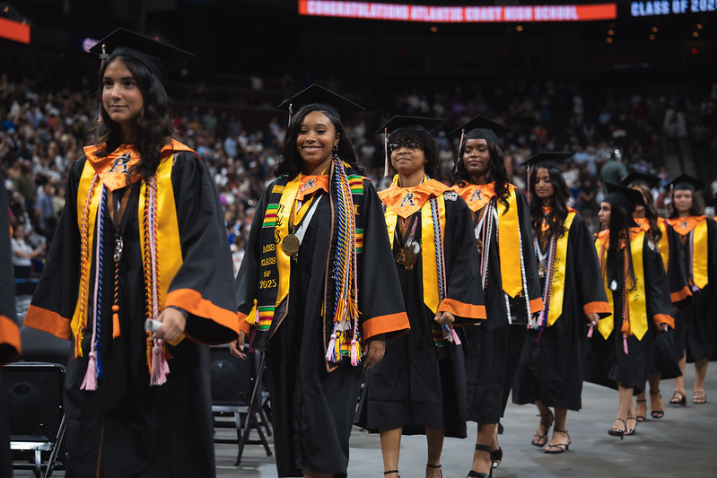 female graduates walking into ceremony with robes and honor cords