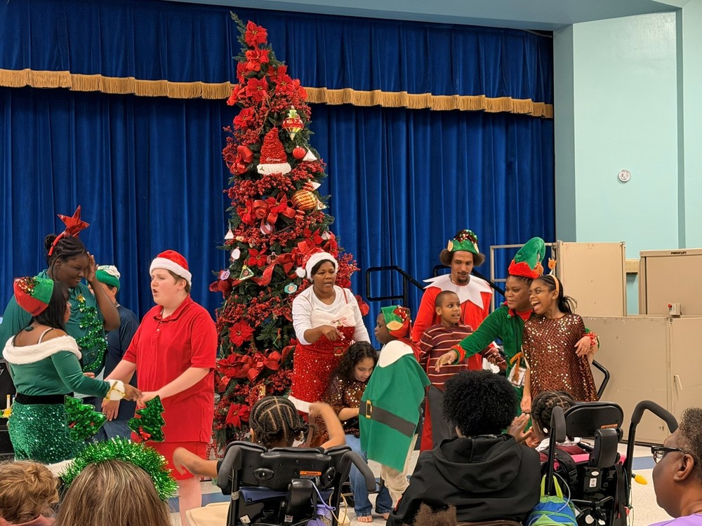 Festive group performing on stage by a Christmas tree.