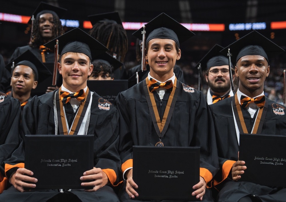 male graduates in cap and gown holding diplomas