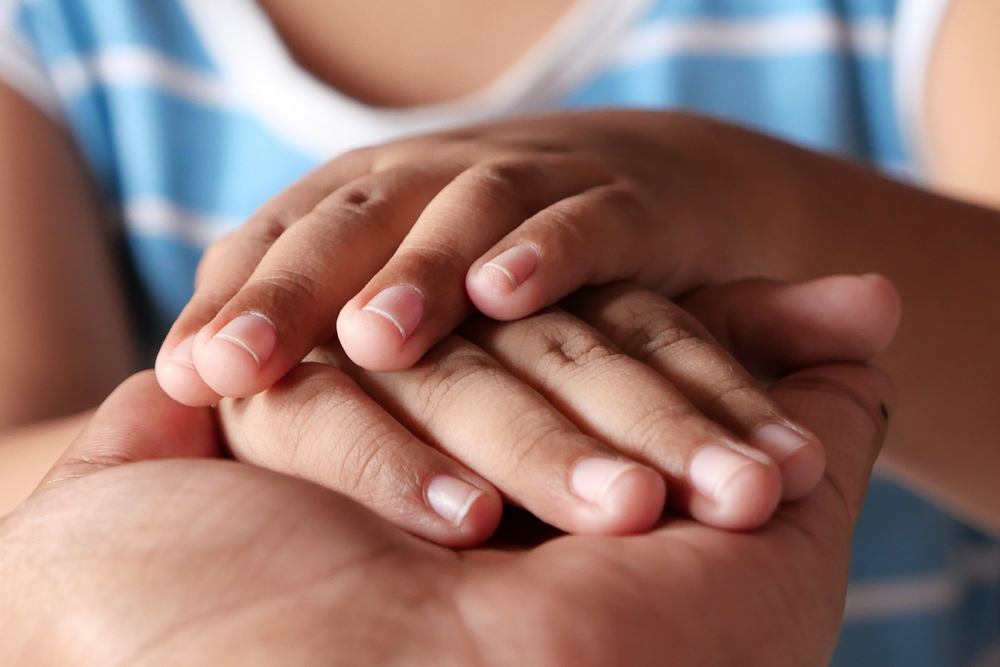 A close up of a child's hand embraced between two adult hands