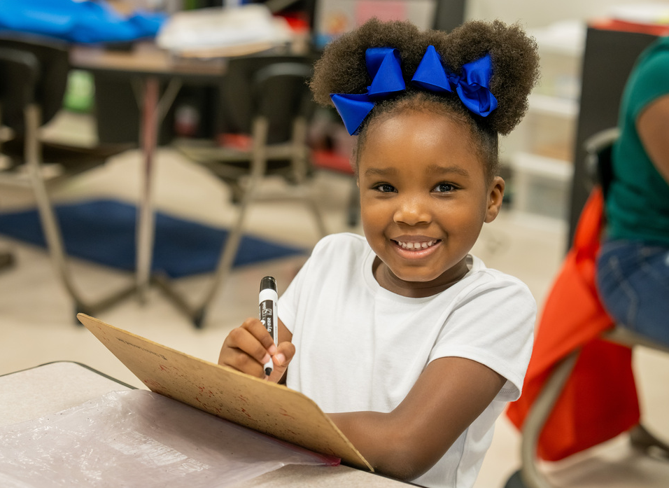 Young girl sitting in classrom desk with dry erase board