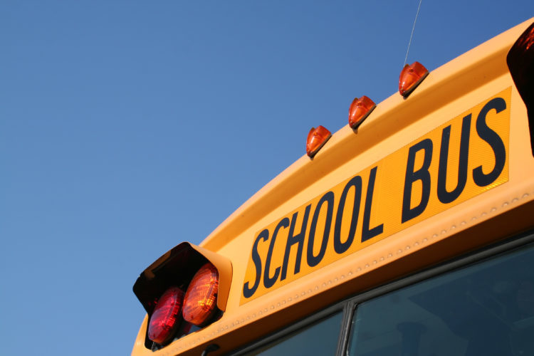 Close up image of a school bus. The words SHOOL BUS above the windshield is visible 