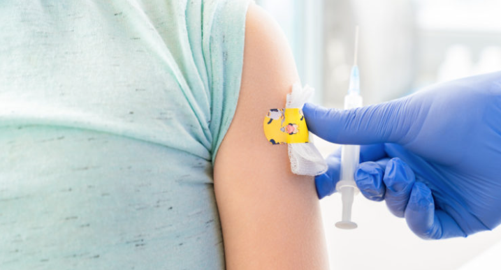 Image of a child receiving a bandaid by a gloved hand also holding a needle