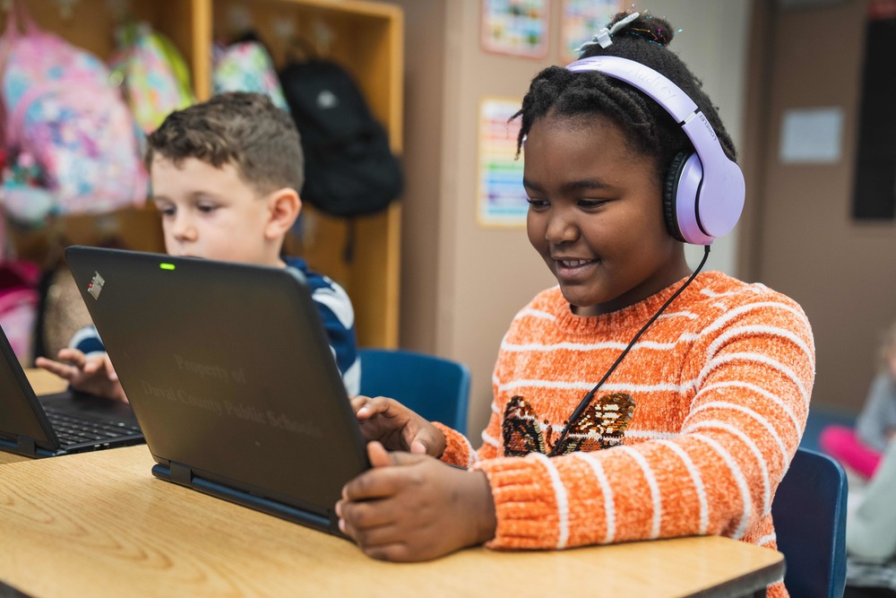 Two students sit with open laptops. Girl in foreground and boy in background
