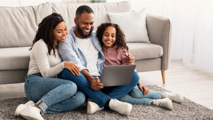 image of a family sitting in front of a coach looking at a laptop smiling