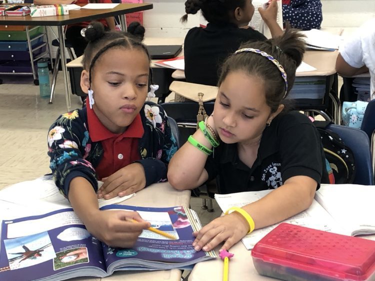 2 students reading a book together in a classrom