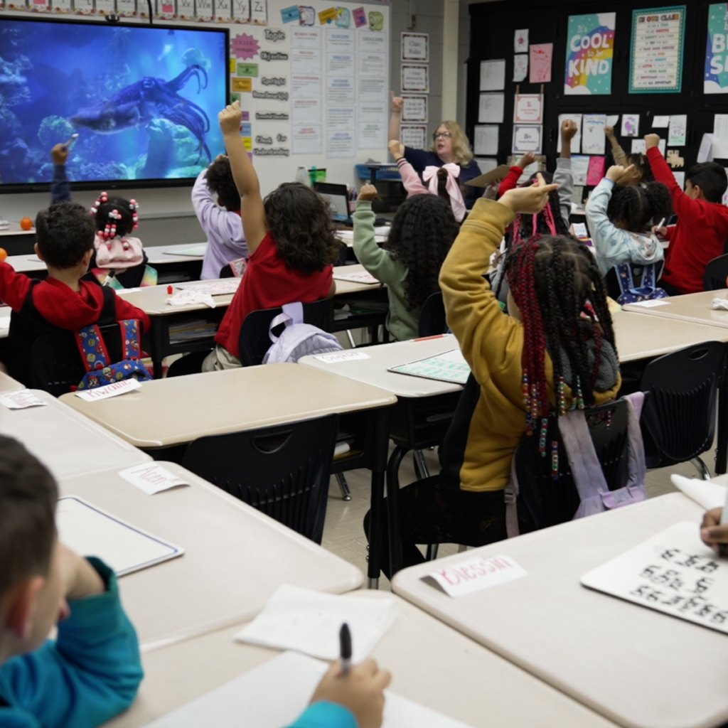 students raising their hands to answer a teacher's question