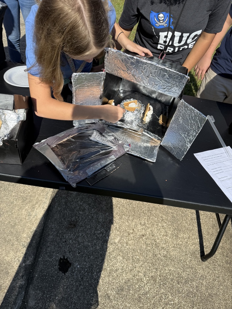 A student adjusts graham crackers inside a foil-lined solar oven while another student watches closely.
