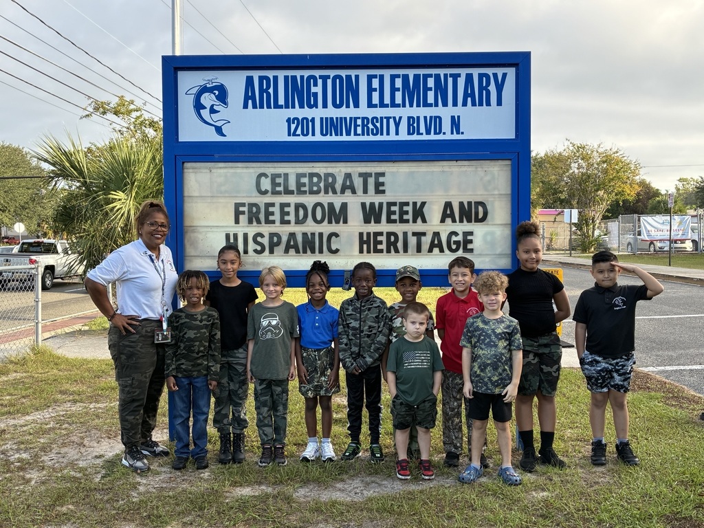 students in camo in front of school sign