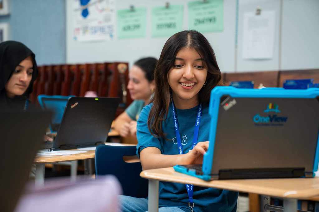 A student smiles as she types on a computer. 